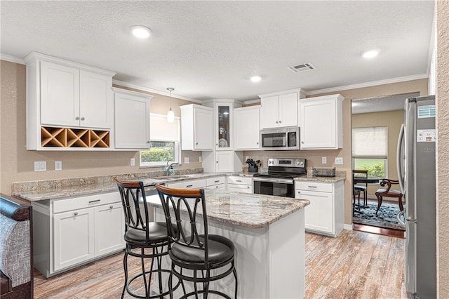 kitchen with hanging light fixtures, ornamental molding, light hardwood / wood-style flooring, and appliances with stainless steel finishes