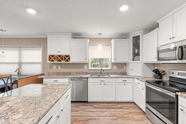 kitchen with light wood-type flooring, white cabinets, pendant lighting, and stainless steel appliances