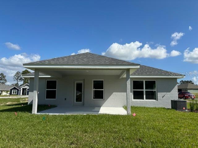 rear view of house with a patio, a yard, stucco siding, and roof with shingles