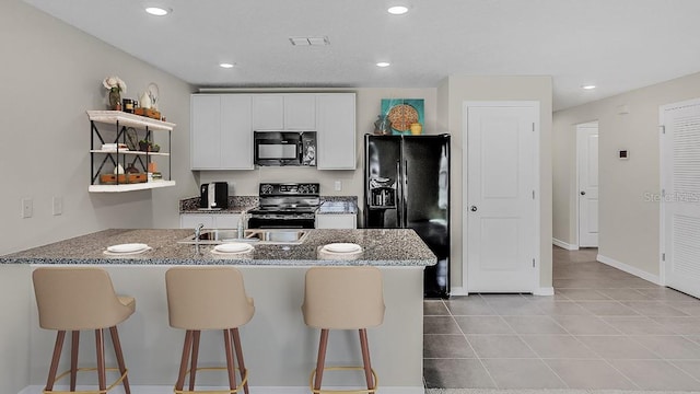 kitchen with light tile patterned floors, a kitchen breakfast bar, black appliances, kitchen peninsula, and white cabinets