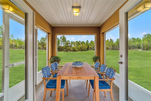 sunroom featuring tile patterned floors, outdoor dining space, and view of wooded area