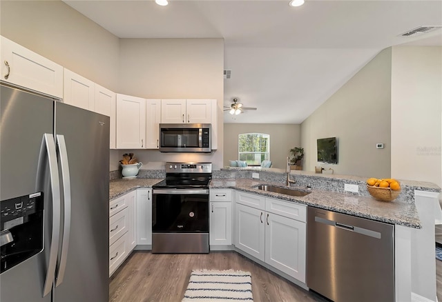 kitchen with appliances with stainless steel finishes, a sink, a peninsula, a ceiling fan, and wood finished floors