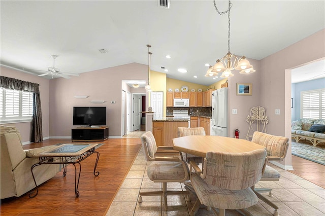 dining space featuring ceiling fan with notable chandelier, lofted ceiling, and light hardwood / wood-style flooring