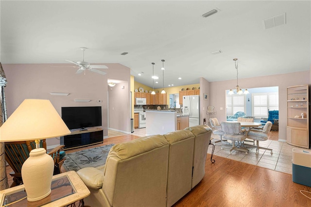 living room featuring ceiling fan with notable chandelier, light wood-type flooring, and vaulted ceiling