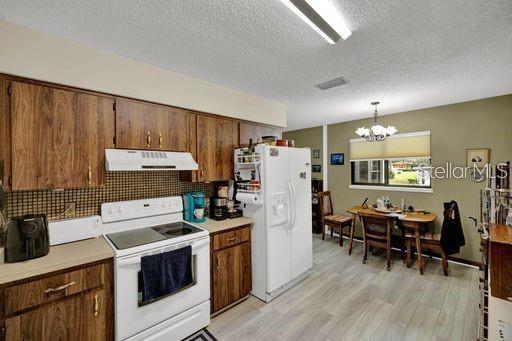 kitchen featuring a textured ceiling, an inviting chandelier, white appliances, pendant lighting, and light hardwood / wood-style floors