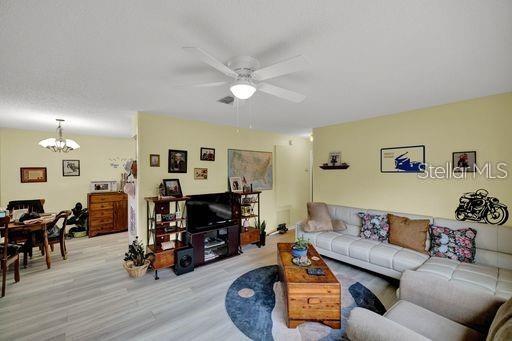 living room with ceiling fan with notable chandelier and light hardwood / wood-style flooring