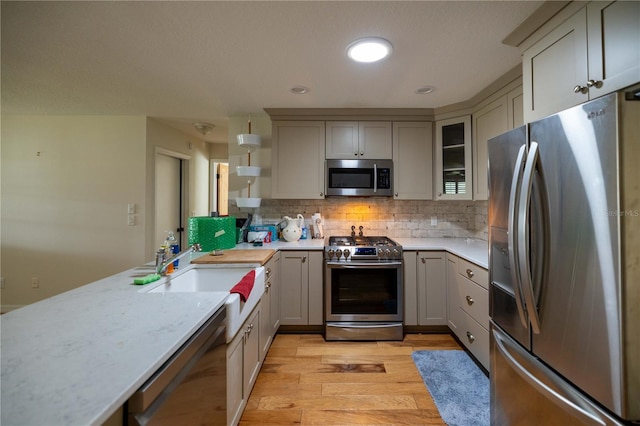 kitchen with light hardwood / wood-style flooring, tasteful backsplash, stainless steel appliances, sink, and gray cabinets