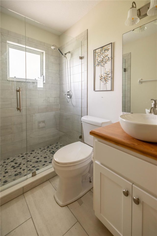 bathroom featuring a shower with shower door, tile patterned flooring, toilet, and vanity