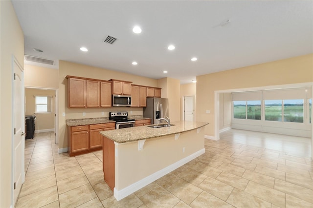 kitchen featuring a kitchen island with sink, a breakfast bar, stainless steel appliances, sink, and light stone counters