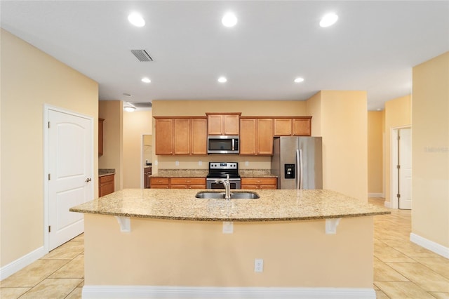 kitchen featuring light stone countertops, light tile patterned floors, stainless steel appliances, and an island with sink