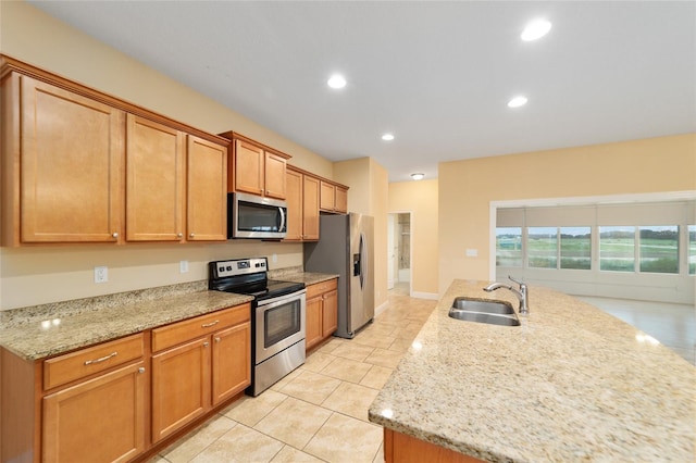 kitchen with light tile patterned floors, light stone counters, stainless steel appliances, sink, and an island with sink