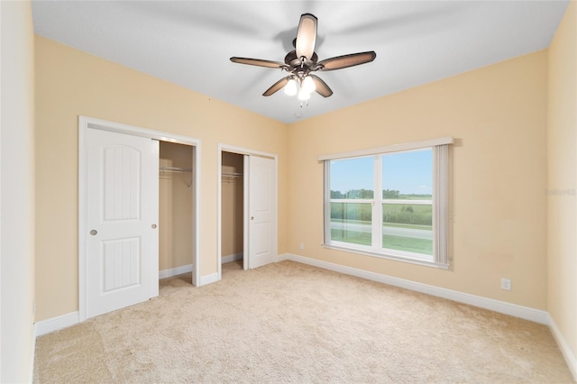 unfurnished bedroom with multiple closets, light carpet, and ceiling fan