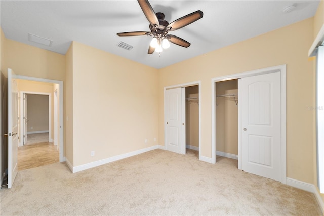 unfurnished bedroom with ceiling fan, light carpet, and multiple closets