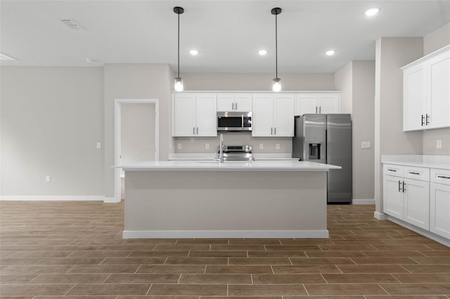 kitchen featuring hanging light fixtures, stainless steel appliances, white cabinets, and a kitchen island with sink