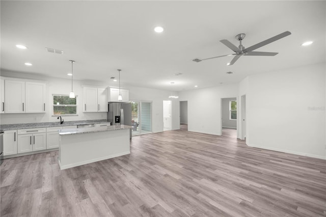 kitchen with a center island, decorative light fixtures, open floor plan, white cabinetry, and light stone countertops