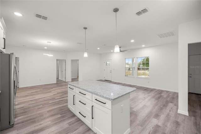 kitchen with open floor plan, freestanding refrigerator, white cabinetry, and pendant lighting