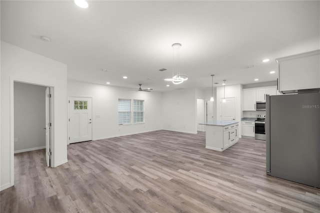 kitchen with stainless steel appliances, white cabinets, open floor plan, a center island, and decorative light fixtures