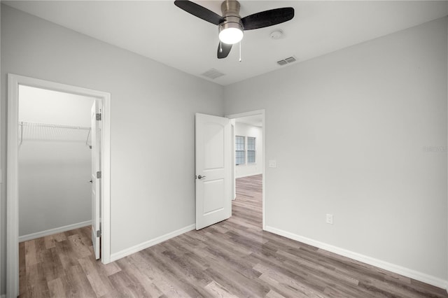 unfurnished bedroom with baseboards, a walk in closet, visible vents, and light wood-style floors