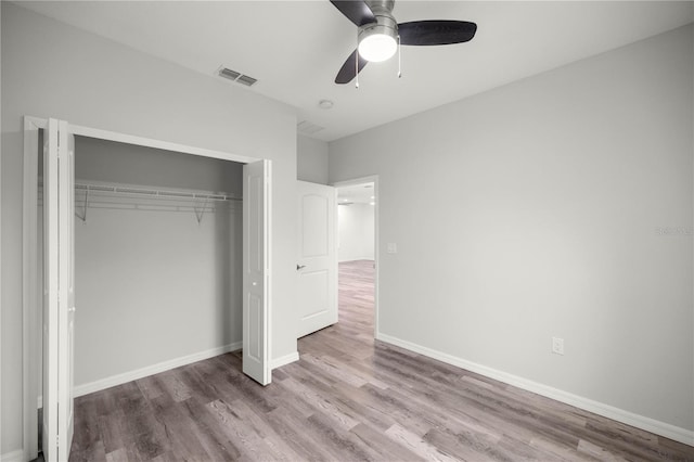 unfurnished bedroom with a closet, visible vents, a ceiling fan, wood finished floors, and baseboards