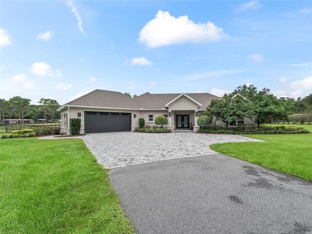 view of front of house featuring decorative driveway, an attached garage, a front lawn, and stucco siding