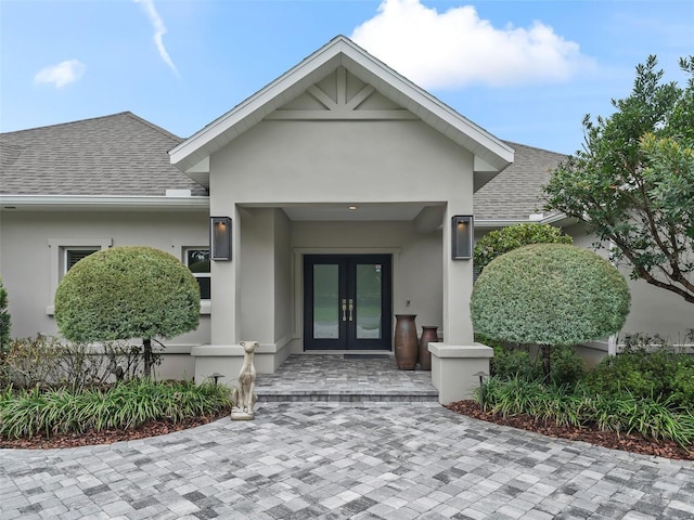 property entrance featuring french doors, roof with shingles, and stucco siding