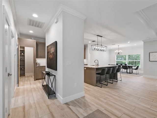 kitchen with a breakfast bar area, visible vents, wood tiled floor, an inviting chandelier, and crown molding