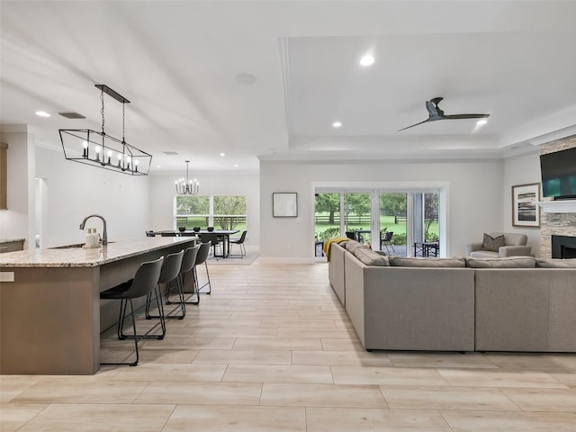 living room with ceiling fan with notable chandelier, sink, and a stone fireplace