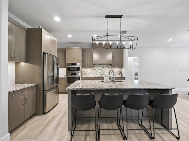 kitchen with sink, light stone countertops, appliances with stainless steel finishes, a center island with sink, and light hardwood / wood-style floors