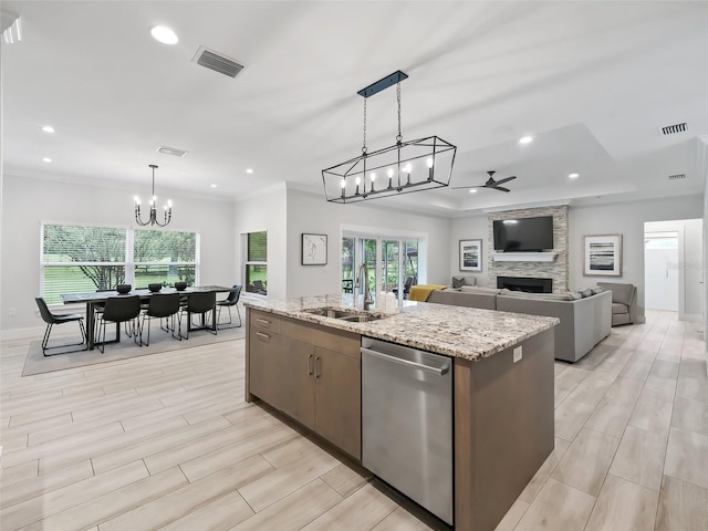 kitchen featuring ceiling fan with notable chandelier, a fireplace, dishwasher, an island with sink, and sink