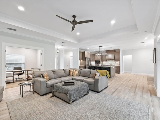 living room with light hardwood / wood-style flooring, a raised ceiling, and ceiling fan with notable chandelier