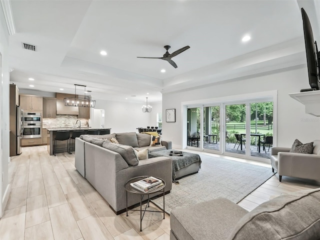 living room with ceiling fan with notable chandelier, a raised ceiling, and sink