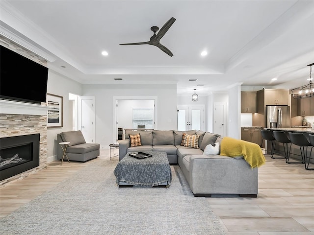 living room with ornamental molding, ceiling fan with notable chandelier, light wood-type flooring, and a tray ceiling