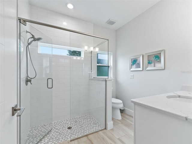 bathroom with wood finish floors, visible vents, toilet, a shower stall, and vanity