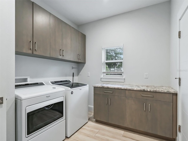 clothes washing area with washer and clothes dryer, cabinet space, and light wood-style floors