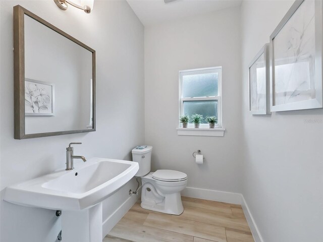 half bathroom featuring a sink, toilet, baseboards, and wood finished floors