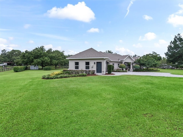 view of front facade featuring a front lawn, fence, stucco siding, an outbuilding, and a storage unit
