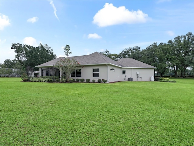 rear view of property featuring a lawn, a shingled roof, and stucco siding