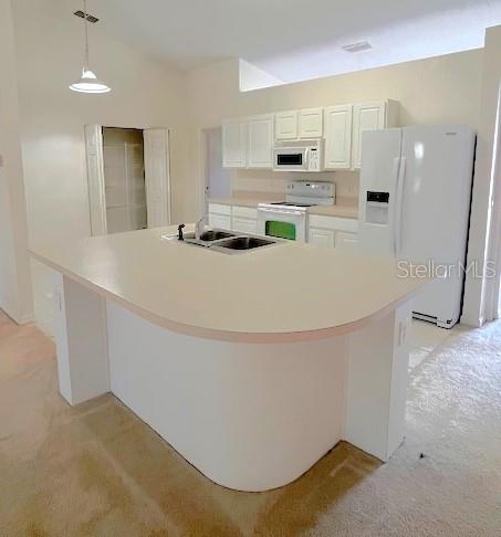 kitchen featuring pendant lighting, a center island, white appliances, white cabinets, and sink