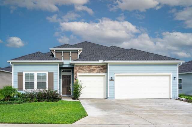 view of front facade with concrete driveway, a front yard, roof with shingles, stone siding, and an attached garage