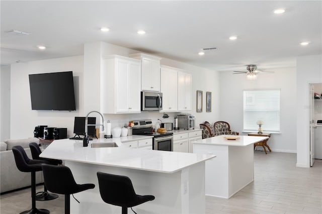 kitchen featuring visible vents, a breakfast bar, a sink, a center island, and appliances with stainless steel finishes