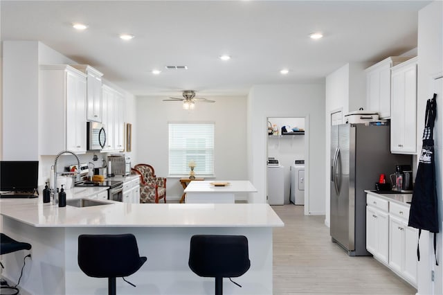 kitchen with ceiling fan, sink, stainless steel appliances, a kitchen bar, and white cabinets