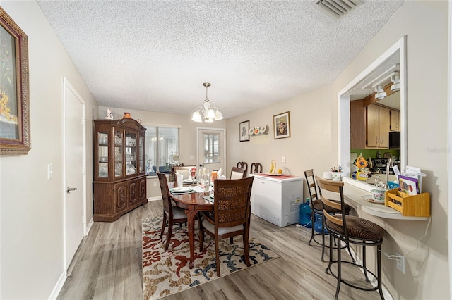 dining space featuring a textured ceiling, an inviting chandelier, and light hardwood / wood-style floors