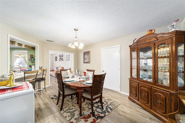 dining space with a textured ceiling, an inviting chandelier, and light hardwood / wood-style floors