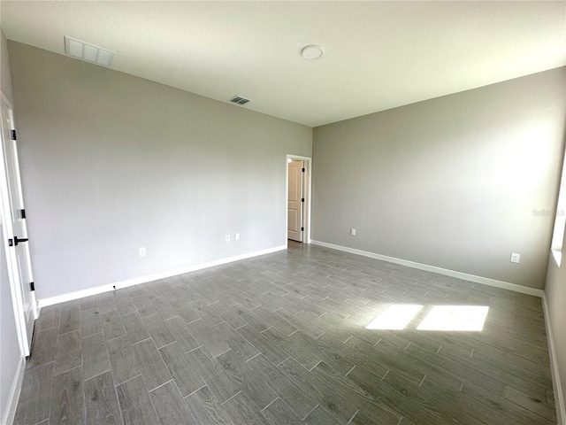 unfurnished room with dark wood-style floors, visible vents, and baseboards