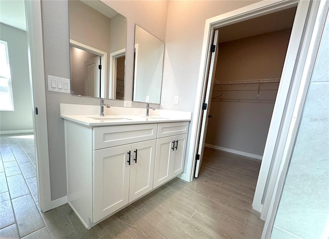 bathroom featuring wood finished floors, a sink, baseboards, a spacious closet, and double vanity