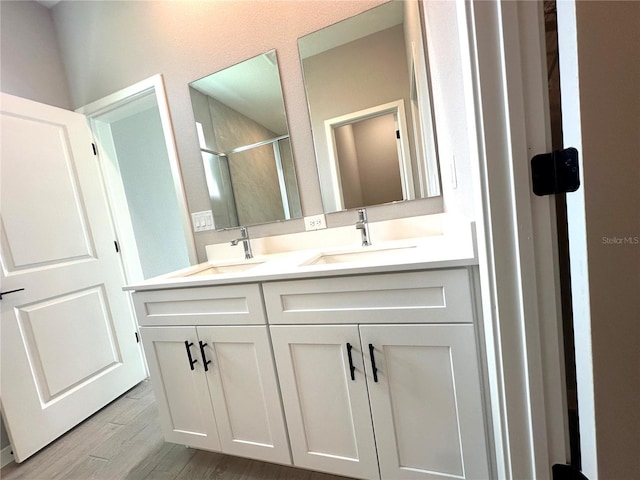 full bath featuring double vanity, a stall shower, a sink, and wood finished floors