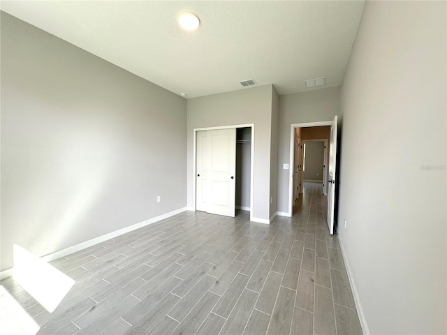 unfurnished bedroom with a closet, wood finished floors, visible vents, and baseboards