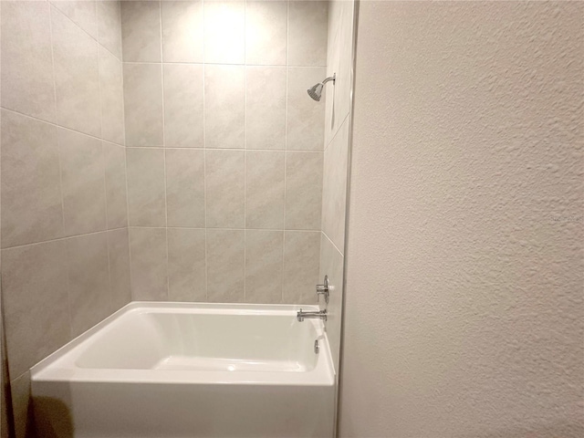 bathroom with a textured wall and tub / shower combination