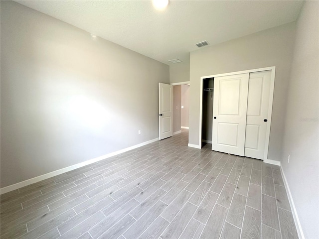 unfurnished bedroom featuring visible vents, baseboards, a closet, and wood finish floors