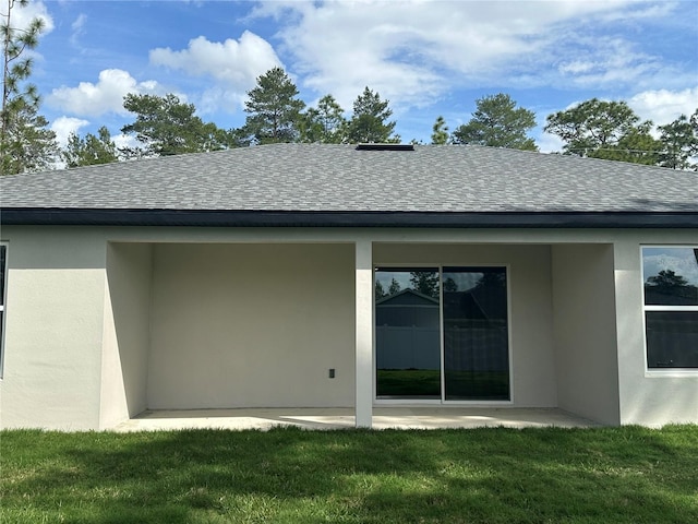 rear view of house featuring a shingled roof, a patio area, a lawn, and stucco siding